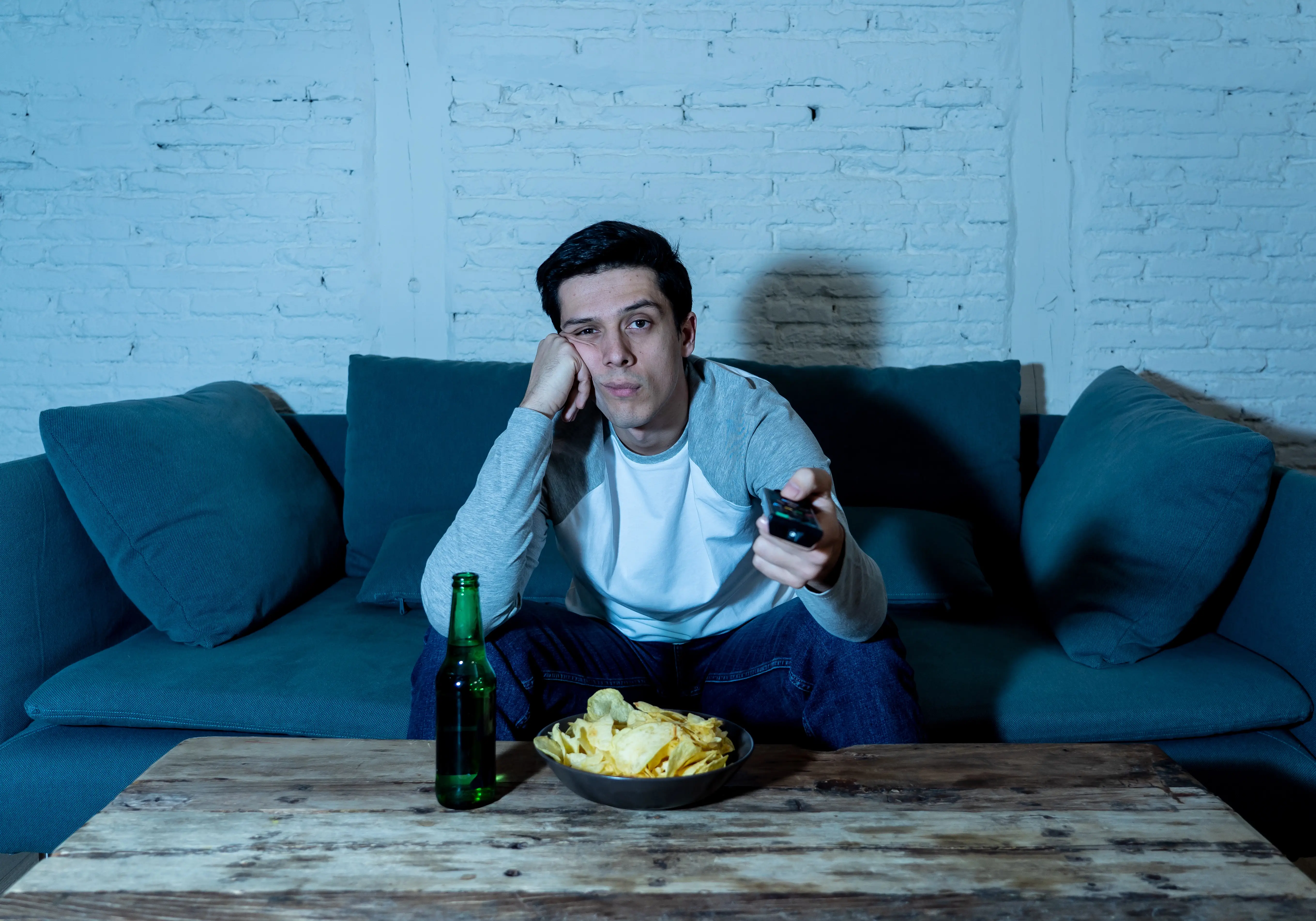 Joven hombre aburrido en el sofá comiendo sin tener buenos hábitos